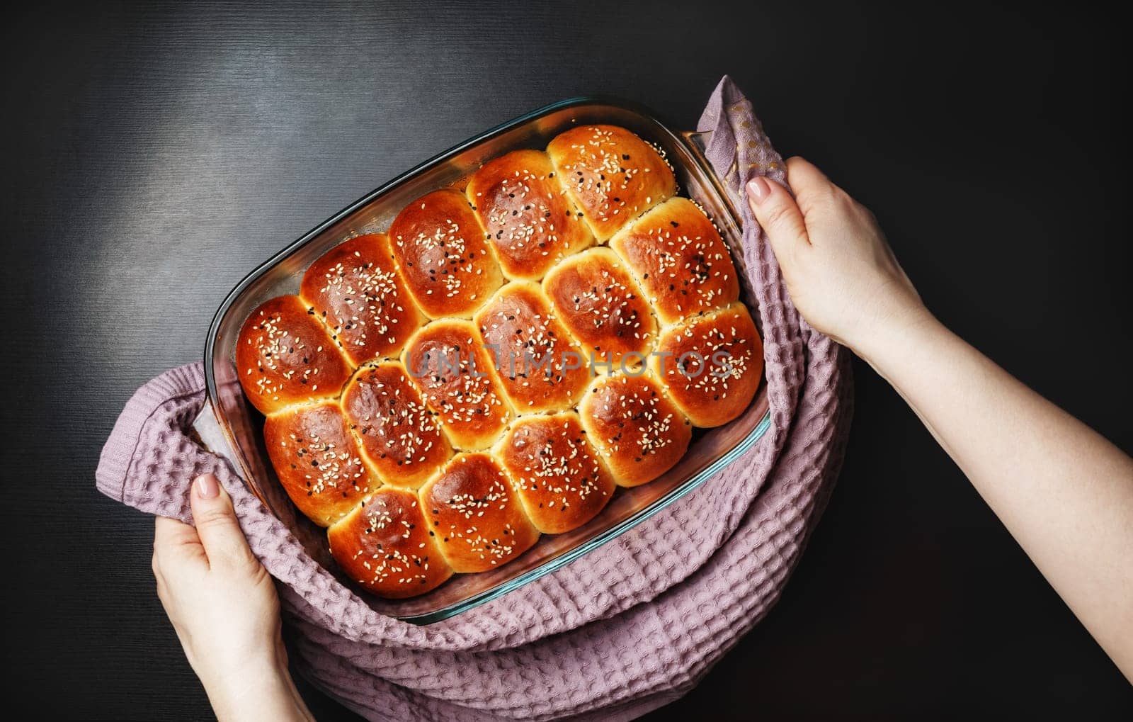 Freshly baked delicious sweet buns with sesame seeds in female hands. Flat lay.