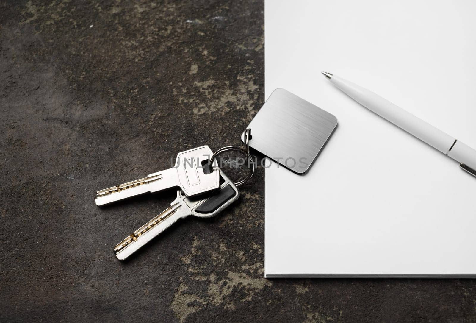House keys, blank keychain, pen and paper on concrete background.