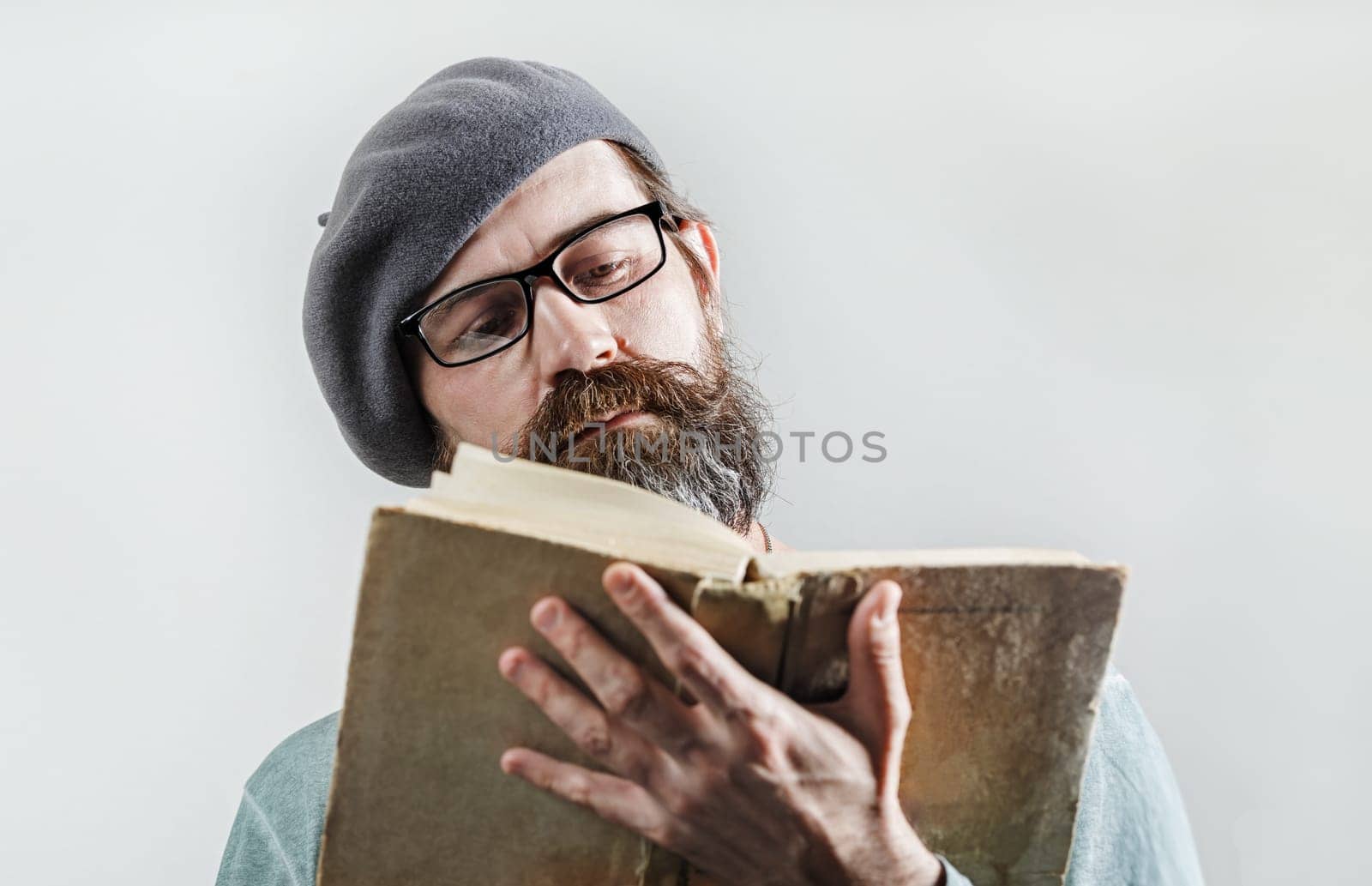 Portrait of serious bearded man in glasses and beret reading old book. Selective focus.