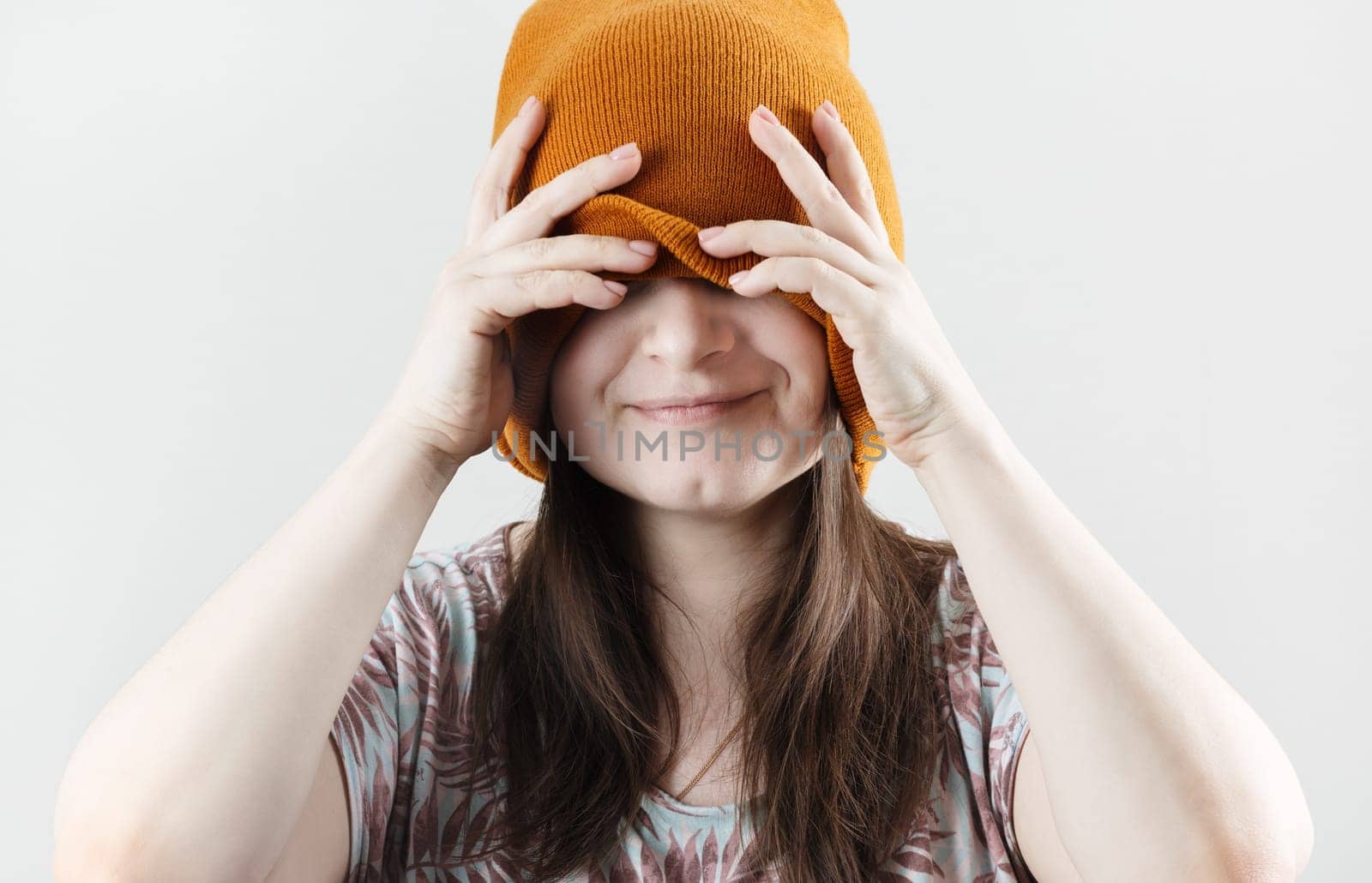Smiling woman covering eyes through knitted hat. Woman hiding face.