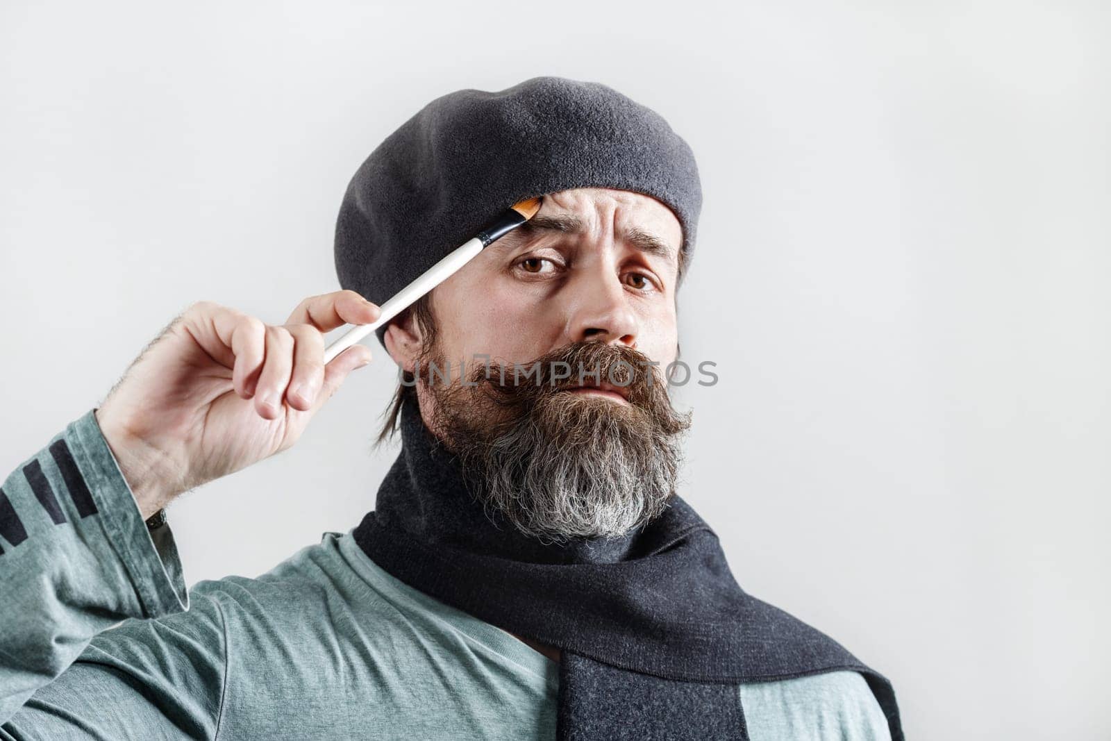 Thoughtful bearded artist. Pensive man in beret with a brush in his hand looks at the camera.
