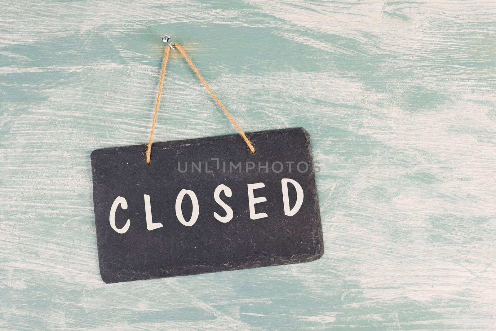 The word closed is standing on a chalkboard sign, hanging on a blue textured weathered door, concept for business, stores and restaurants