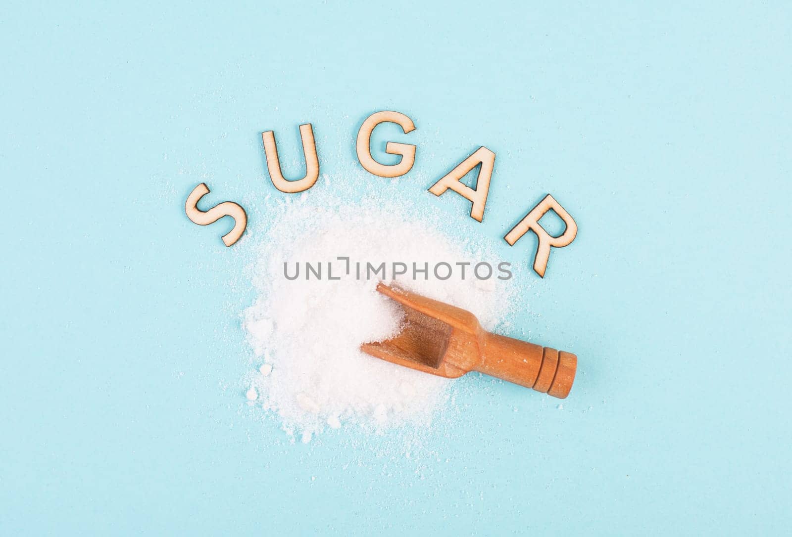 Heap of refined sugar, unhealthy food and lifestyle, ingredients for baking, wooden shovel, isolated on a blue colored background