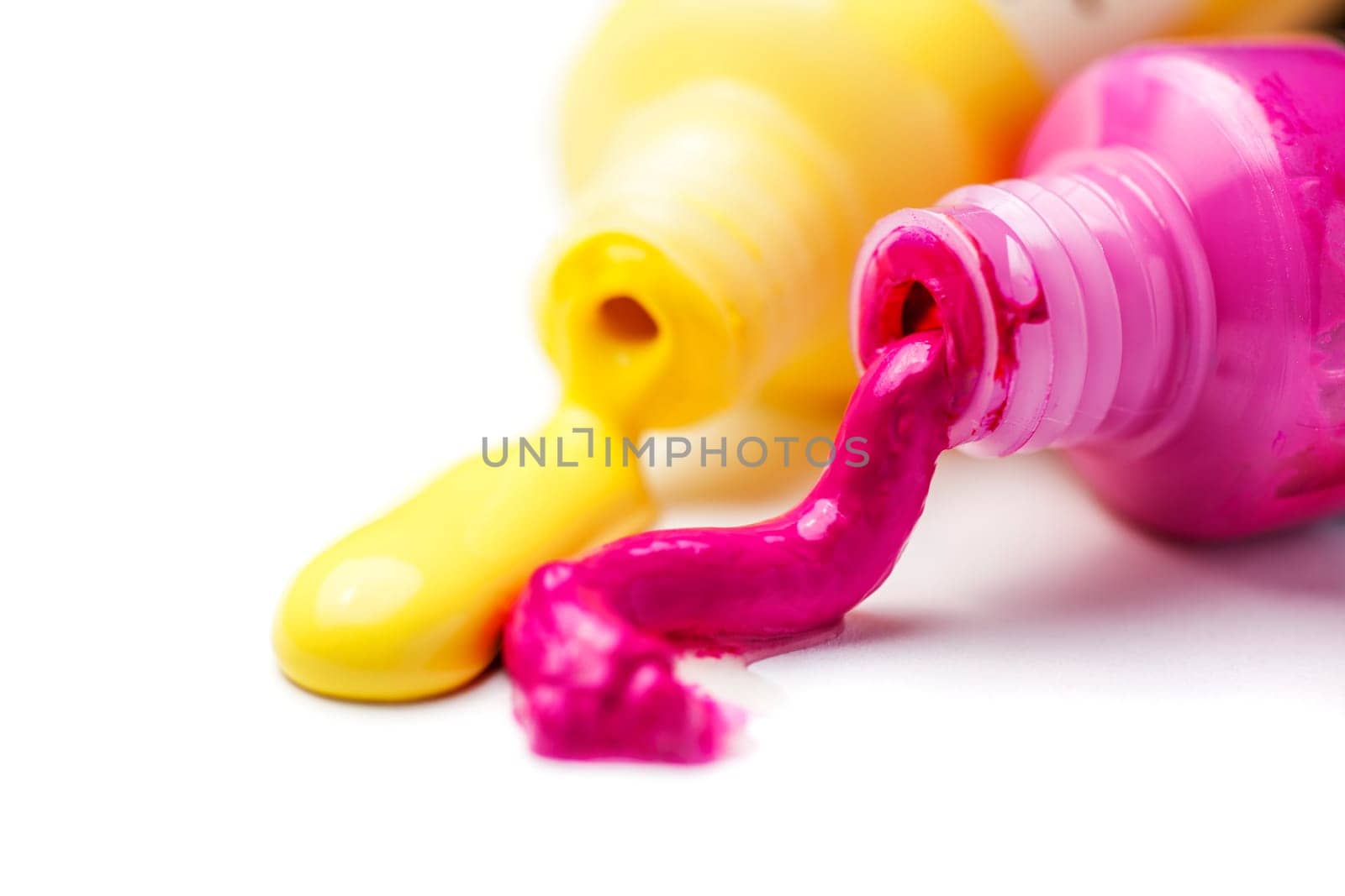 Close-up of two open tubes with magenta and yellow artists' paint spilling out on a white background.