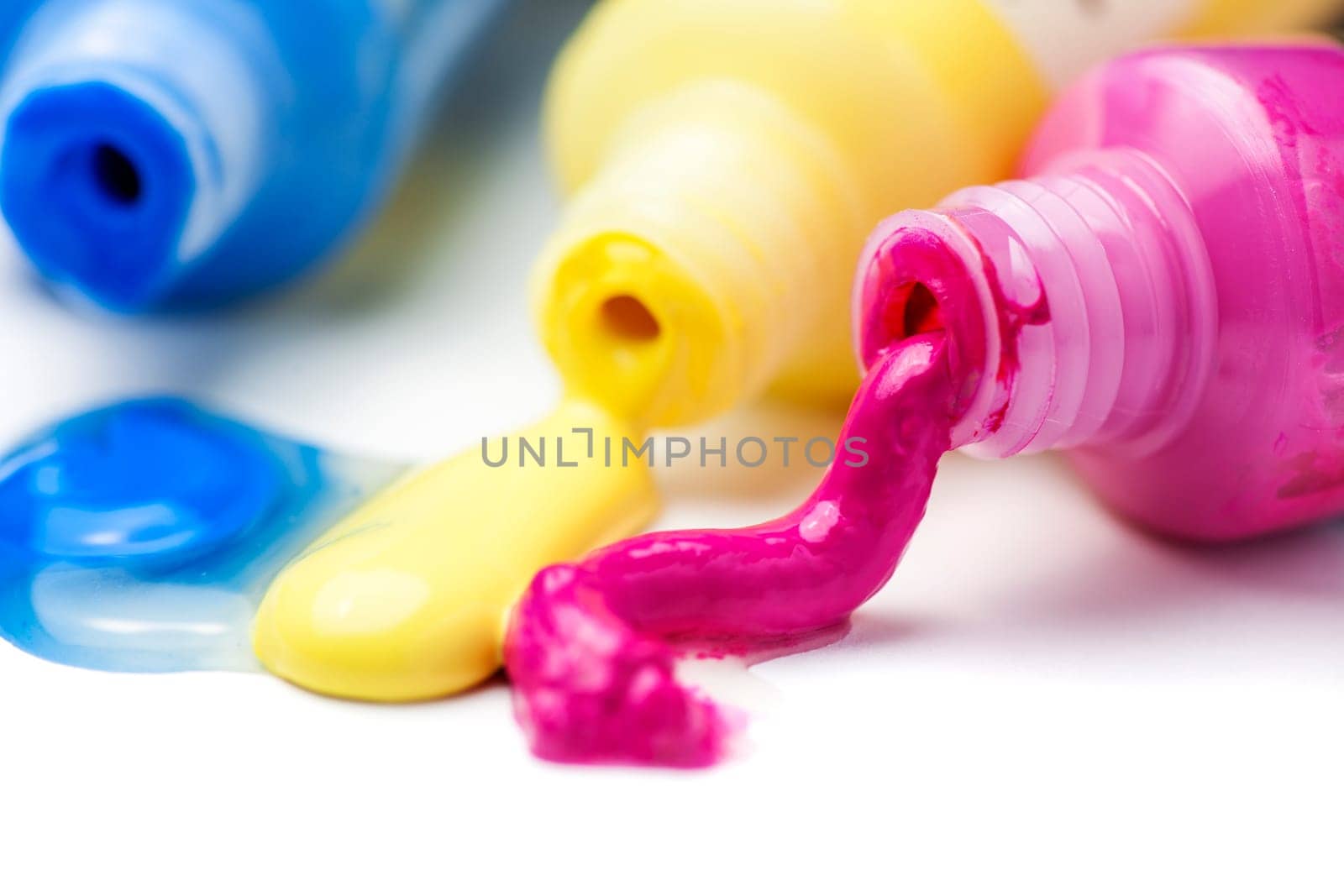 Close-up of three open tubes with magenta, yellow and blue artist paints spilling out on a white background.