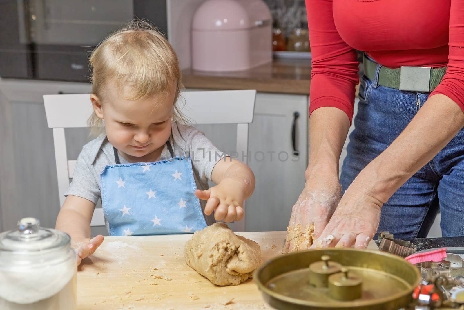 Adorable funny blond little child boy helps in preparing the dough in domestic kitchen.