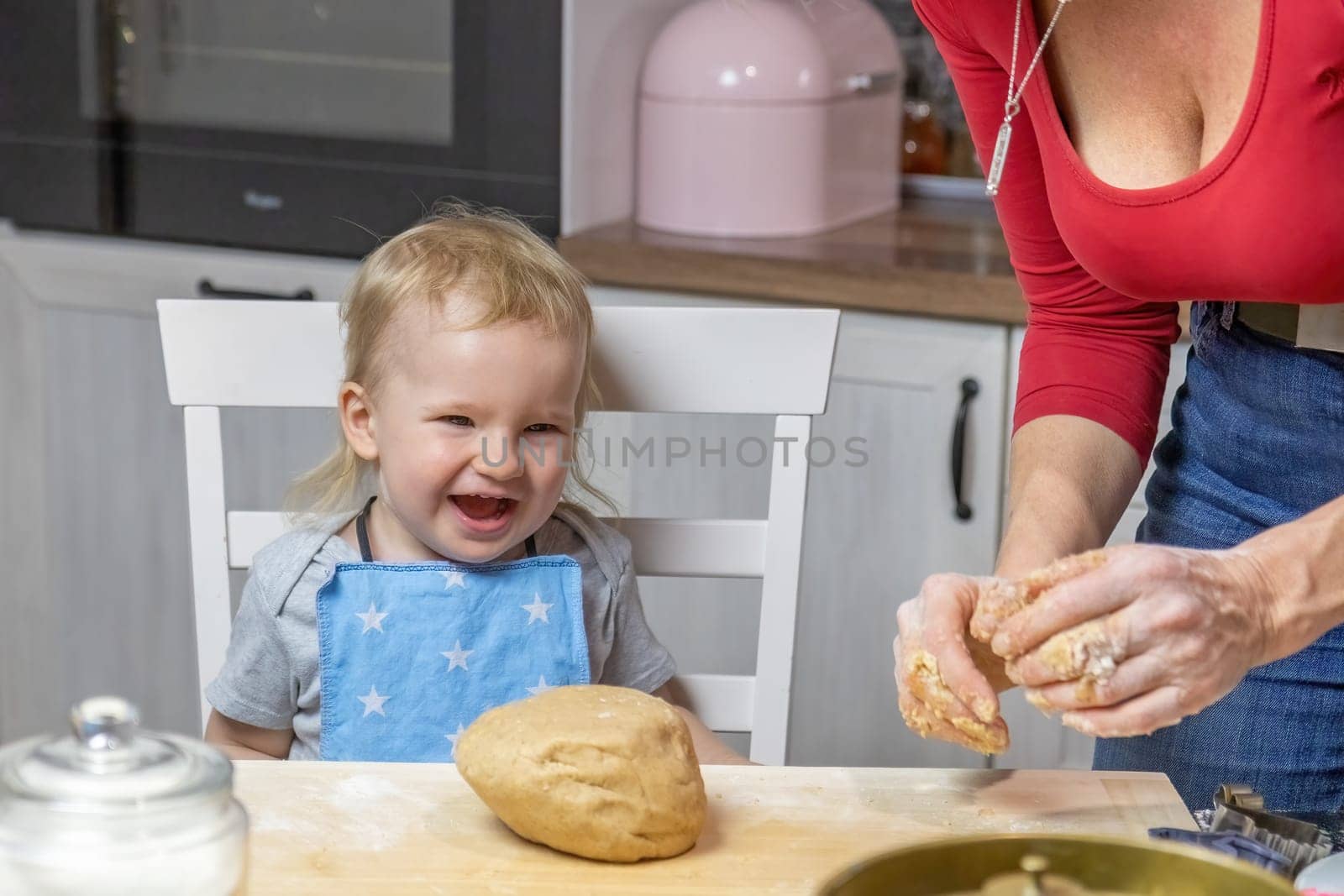 Smiling adorable funny blond little child boy is baking cake in domestic kitchen. Horizontally.