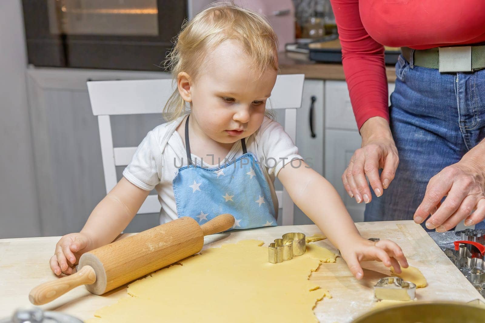 Adorable funny little child boy is taking a heart to make pastries in the kitchen. Horizontally.