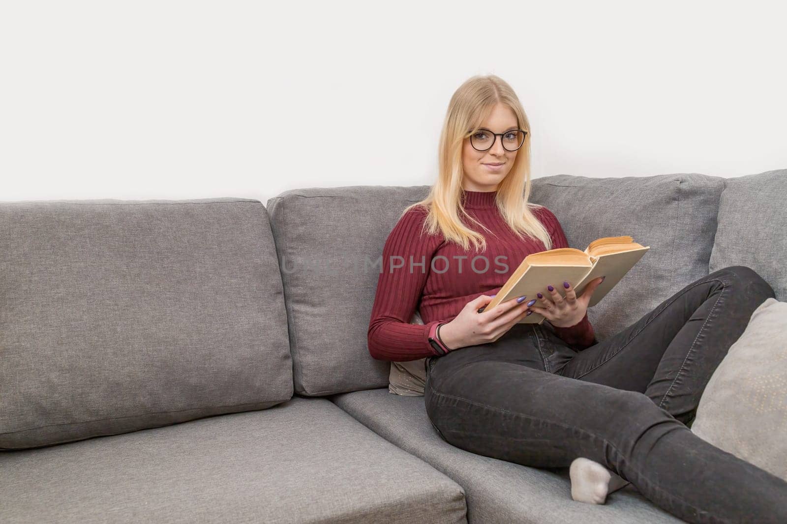 Young woman is sitting on the couch and reading a book. Horizontally.