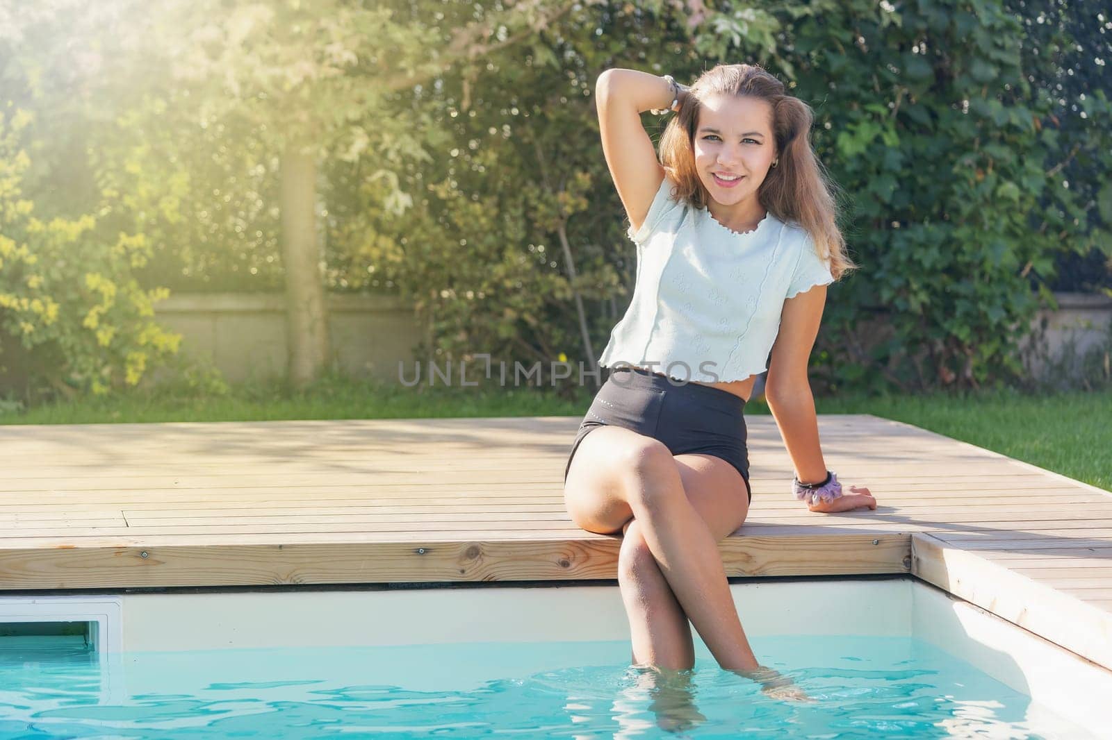 Cute tanned girl is posing with feet in the pool. Horizontally.