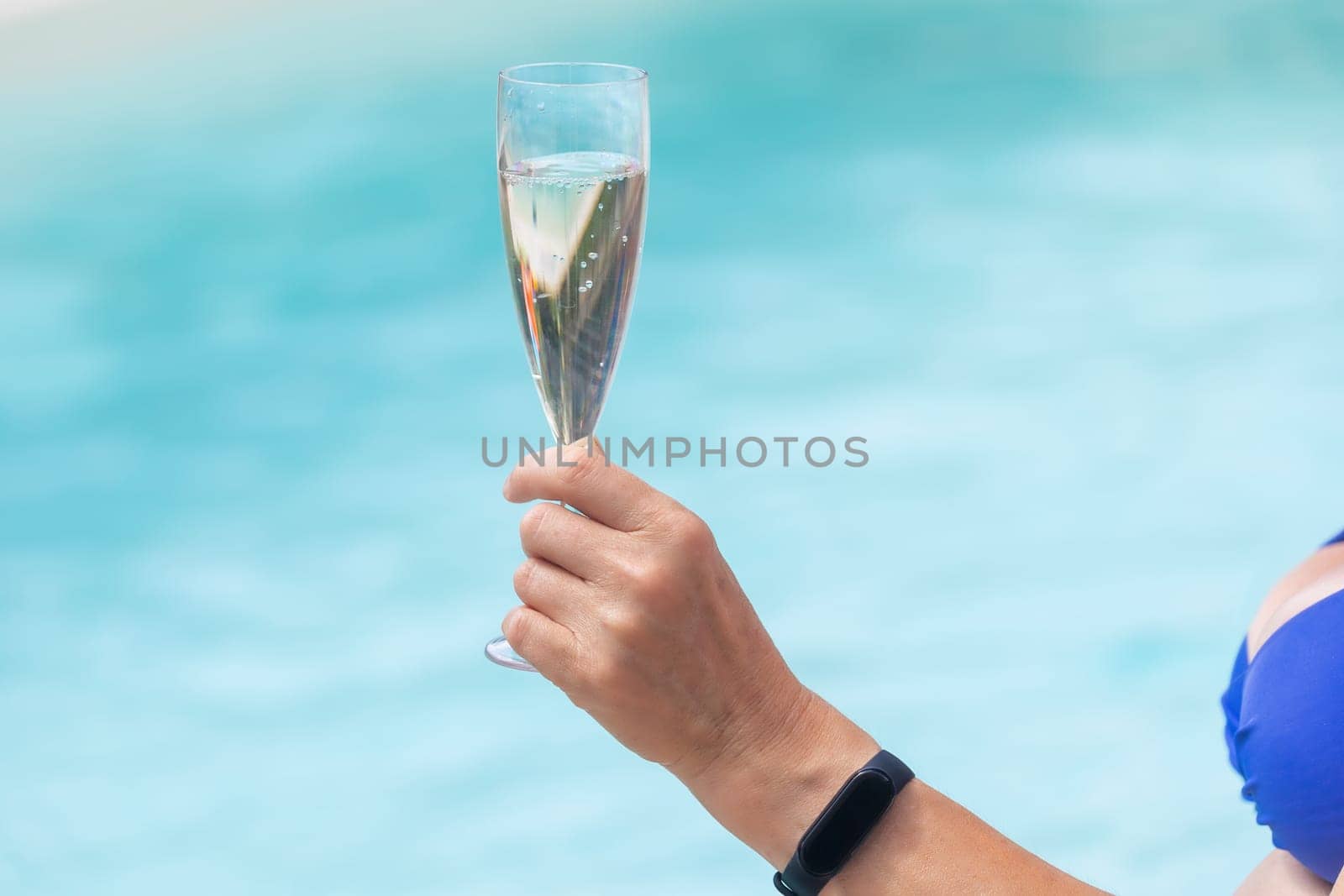Woman is holding champagne glass in the pool closeup.  Horizontally.