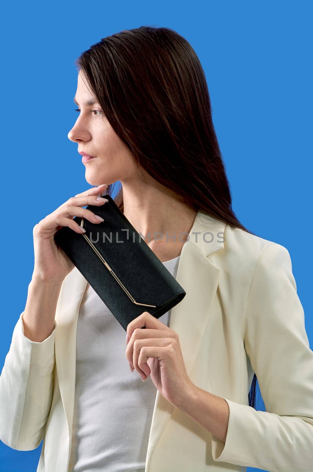 A beautiful young woman is holding a black handbag on a blue background. High quality photo