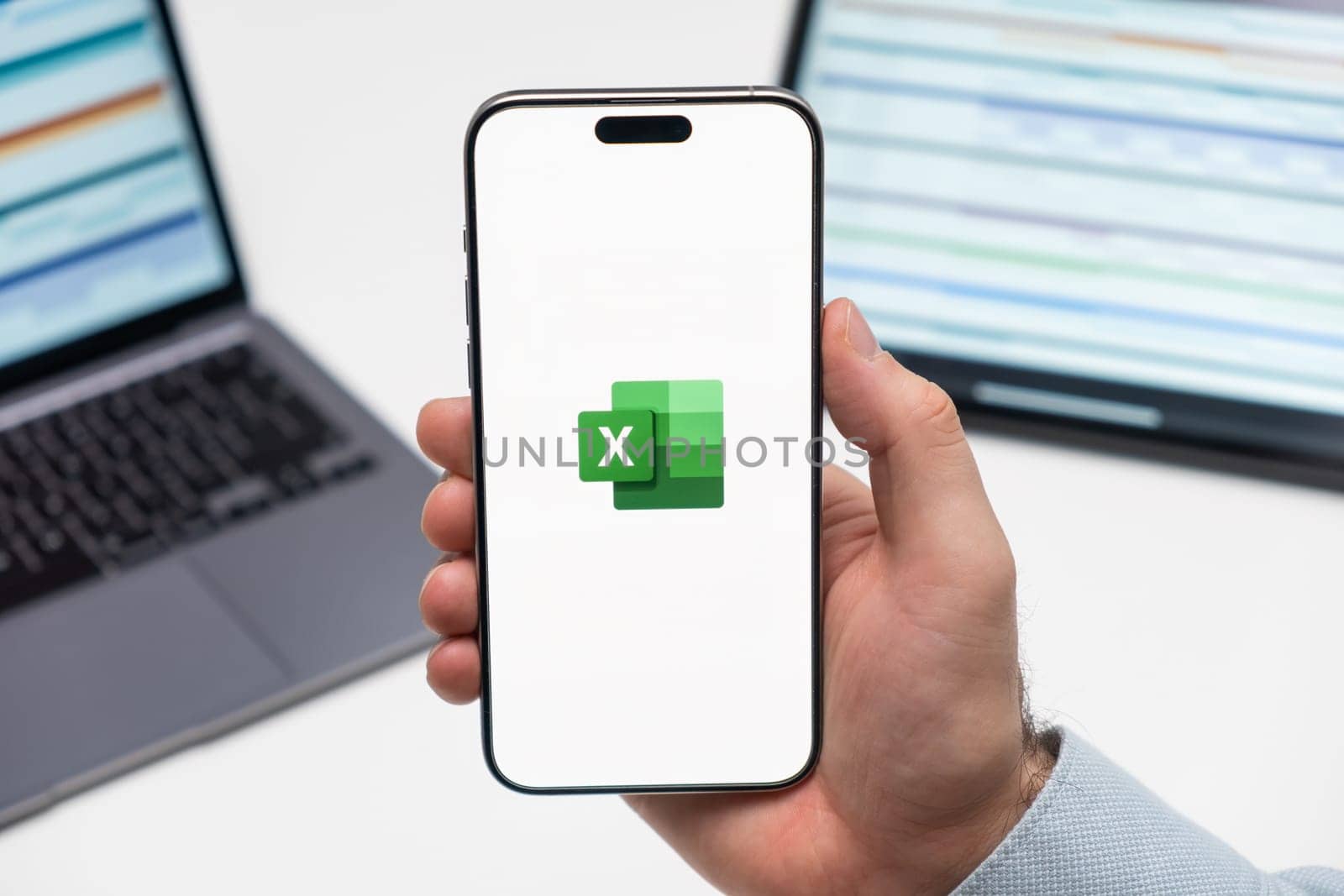 PRAGUE, CZECHIA - JULY, 2024: Excel logo on the screen of smartphone in mans hand and laptop on the background