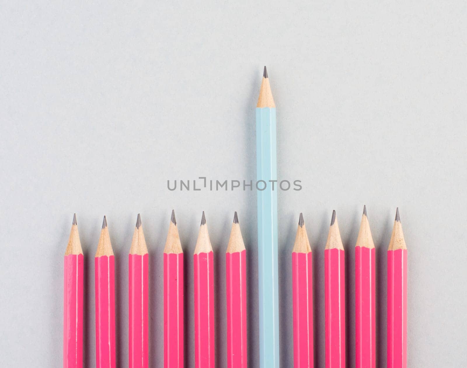 Pink pencils in a row, one blue pen is standing out, be different, leadership and teamwork concept