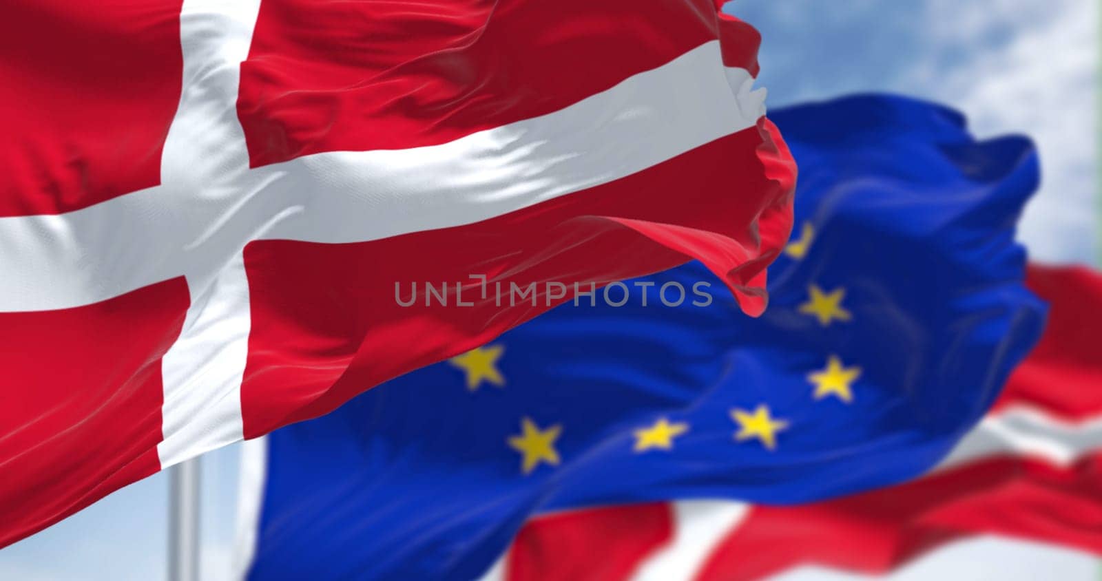 Detail of the national flag of Denmark waving in the wind with blurred european union flag in the background on a clear day. Democracy and politics. European country. Selective focus.
