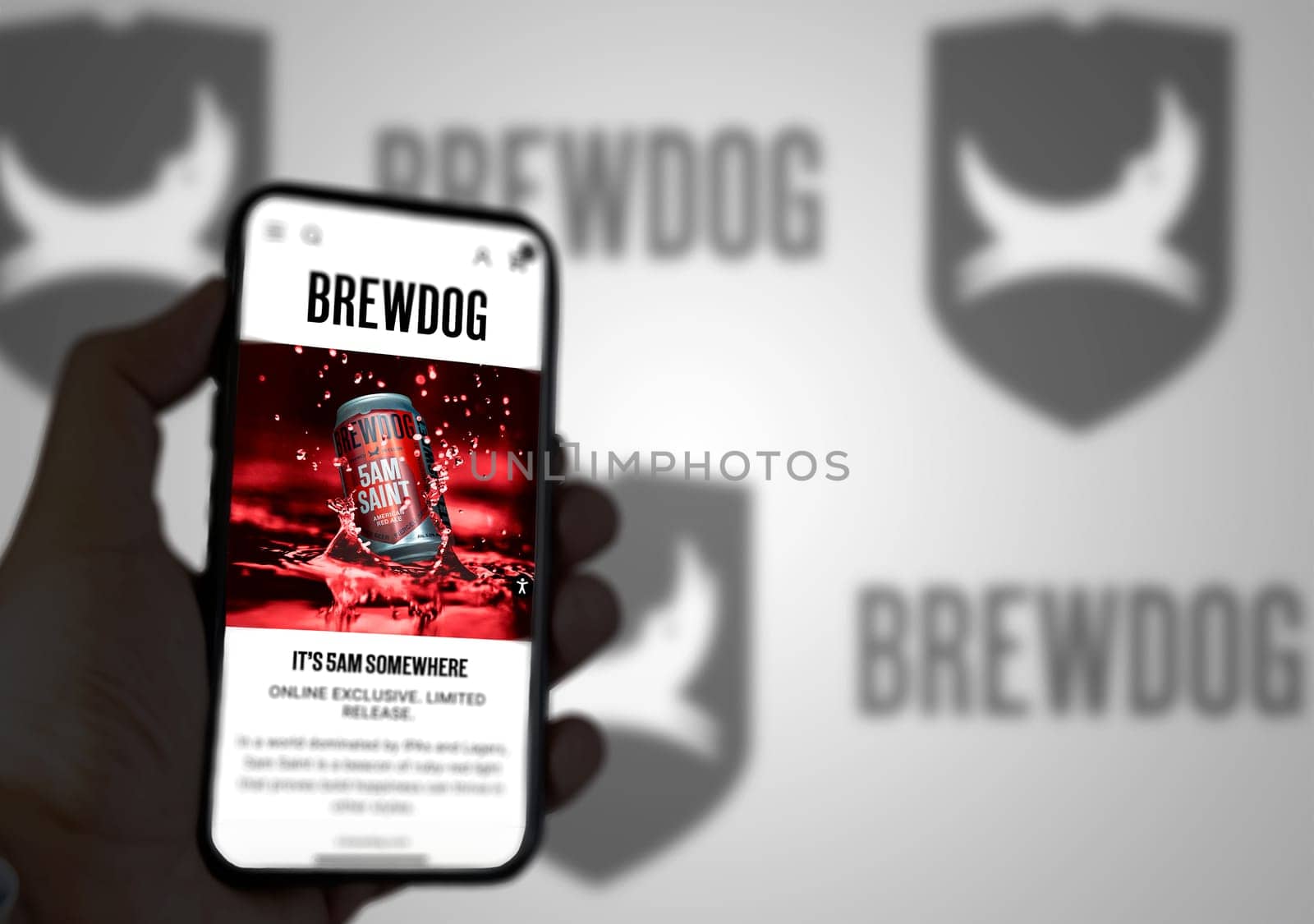 Ellon, Scotland, April 2022: The home page of the site Brewdog on the screen of a mobile phone. The mobile phone is held by a male hand. The company logo is blurry on the green background.