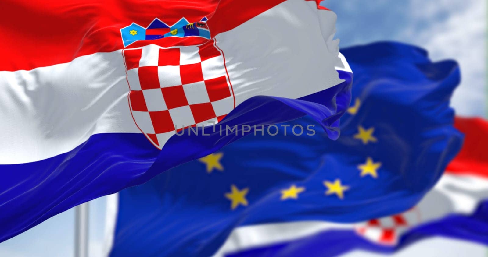 Detail of the national flag of Croatia waving in the wind with blurred european union flag in the background on a clear day. Democracy and politics. European country. Selective focus.