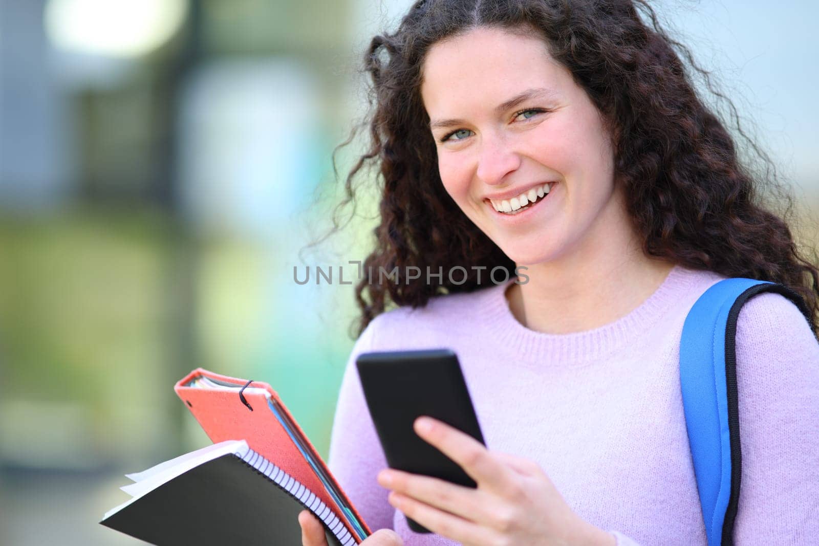 Happy student looking at camera holding phone