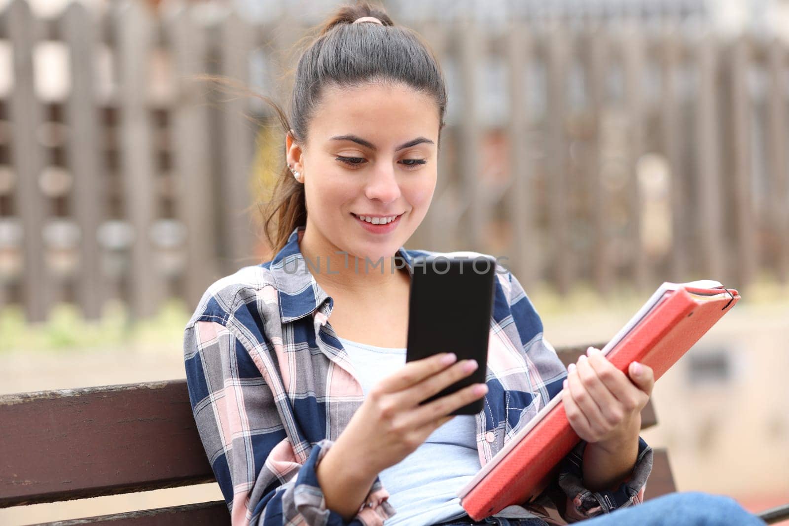 Happy student checking smartphone in a bench
