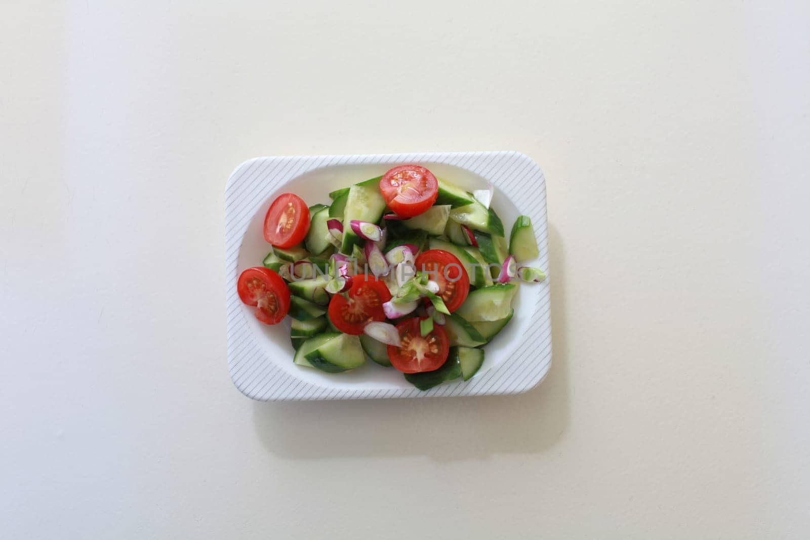 salad of fresh cucumbers, cherry tomatoes and green onions on a square dish