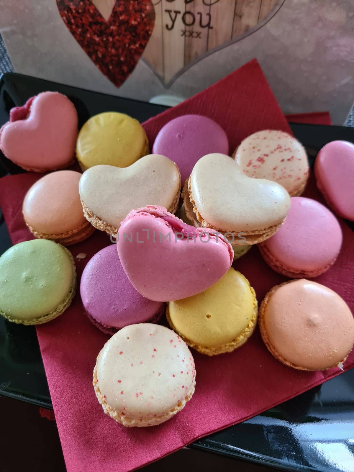 Top view of three delicious macarons and love heart symbol on napkin on wooden table. Romantic vintage valentines day and wedding background