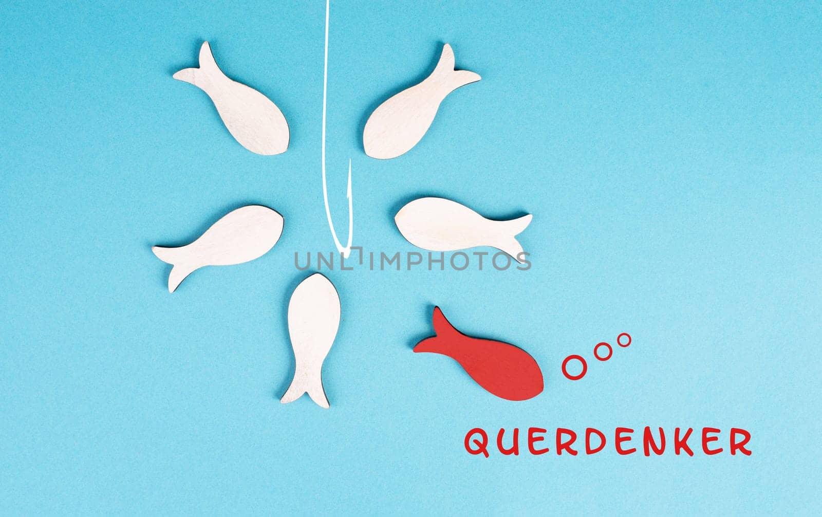 Think different stands in german language on the blue background, red fish is standing out from the crowd, being a nonconformist, conspiracy theory, group swims to the fishing rod