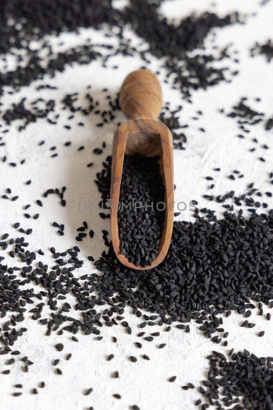 Wooden scoop of Indian spice Black cumin (nigella sativa or kalonji) seeds close up on white table. Traditional asian medicine, healthy eating, vegetarian and vegan food concept