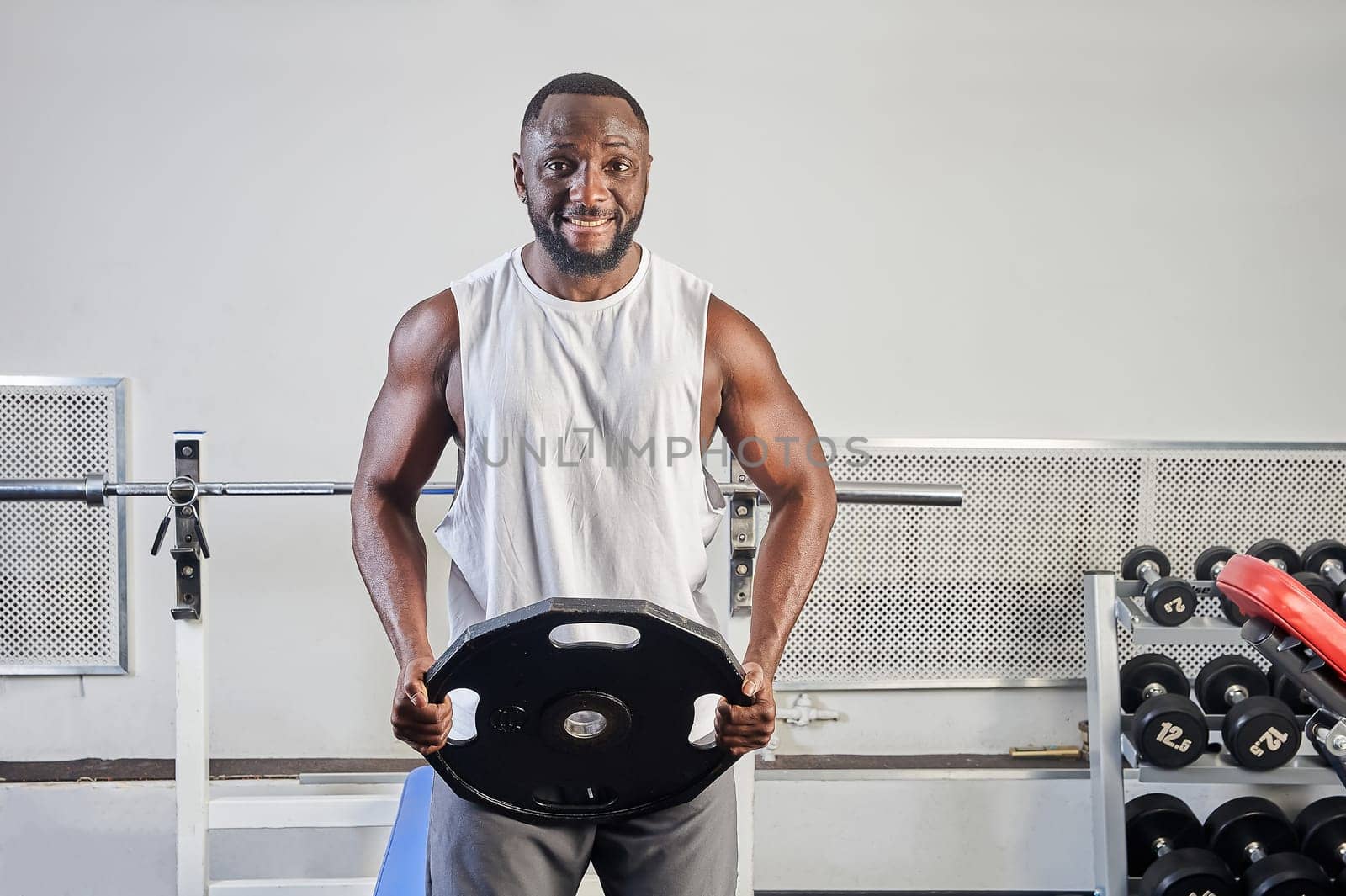 An African-American man in the gym holds a metal pancake in his hands. High quality photo