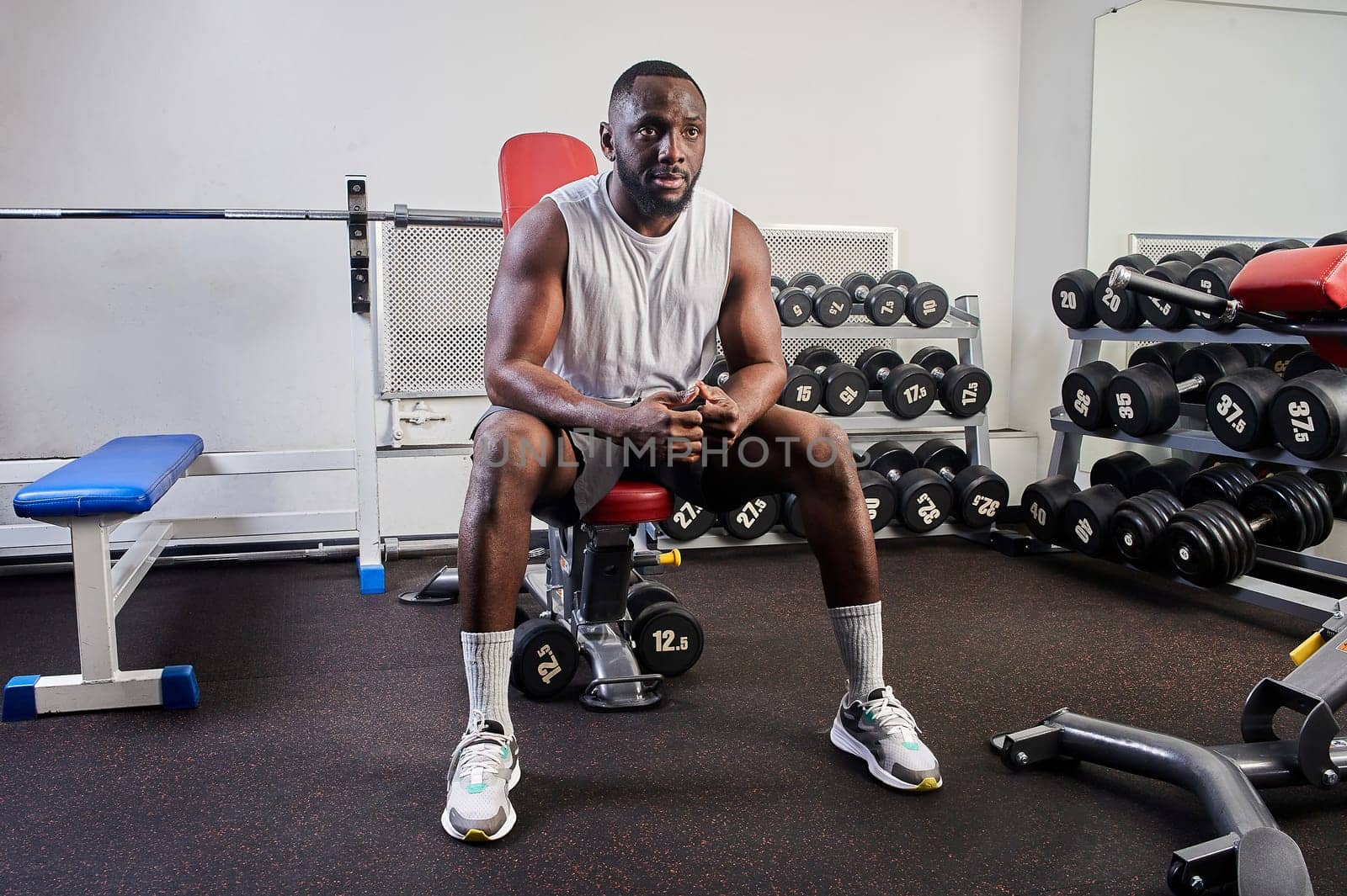 An African-American man is sitting on a bench bench in the gym and resting. High quality photo