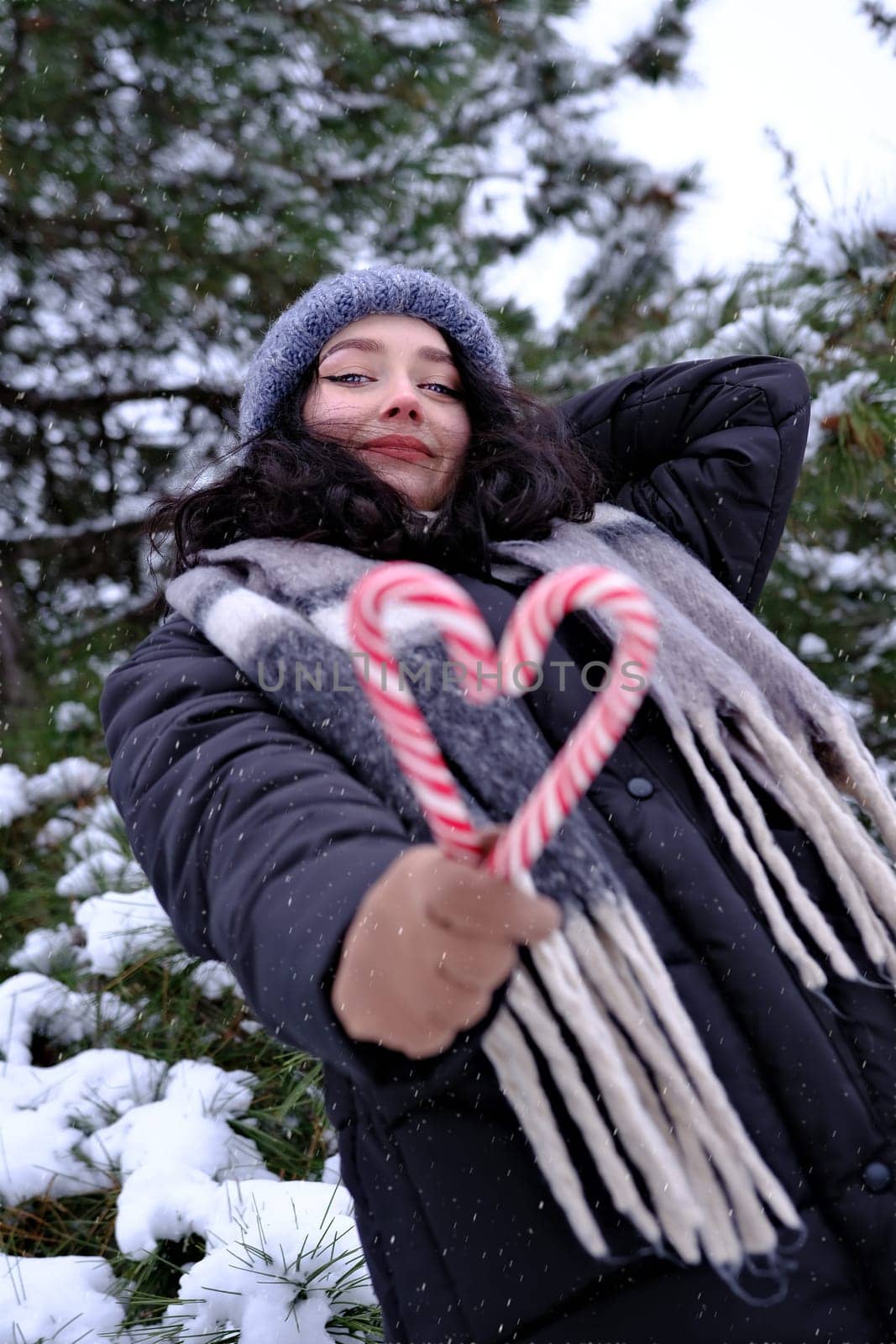 Woman in winter time holding two candy canes forming a heart in her hand outdoor