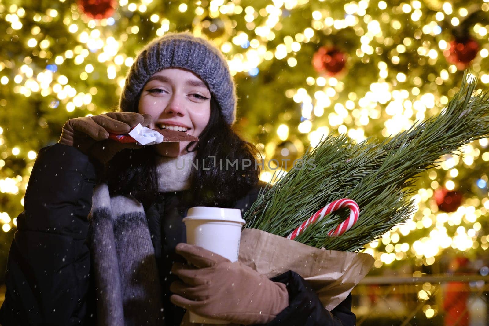 young beautiful happy Face of smiling girl posing. Christmas tree on background. Happy New Year eating Chocolate with coffee cup and candy