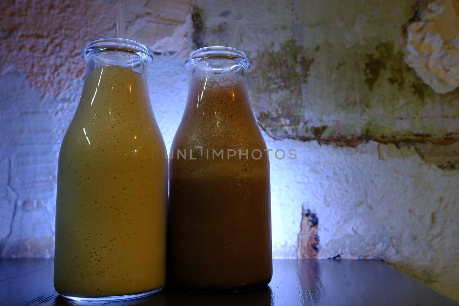 Milkshake chocolate milk in bottles with straws vintage blue neon lighted background closu up side view.