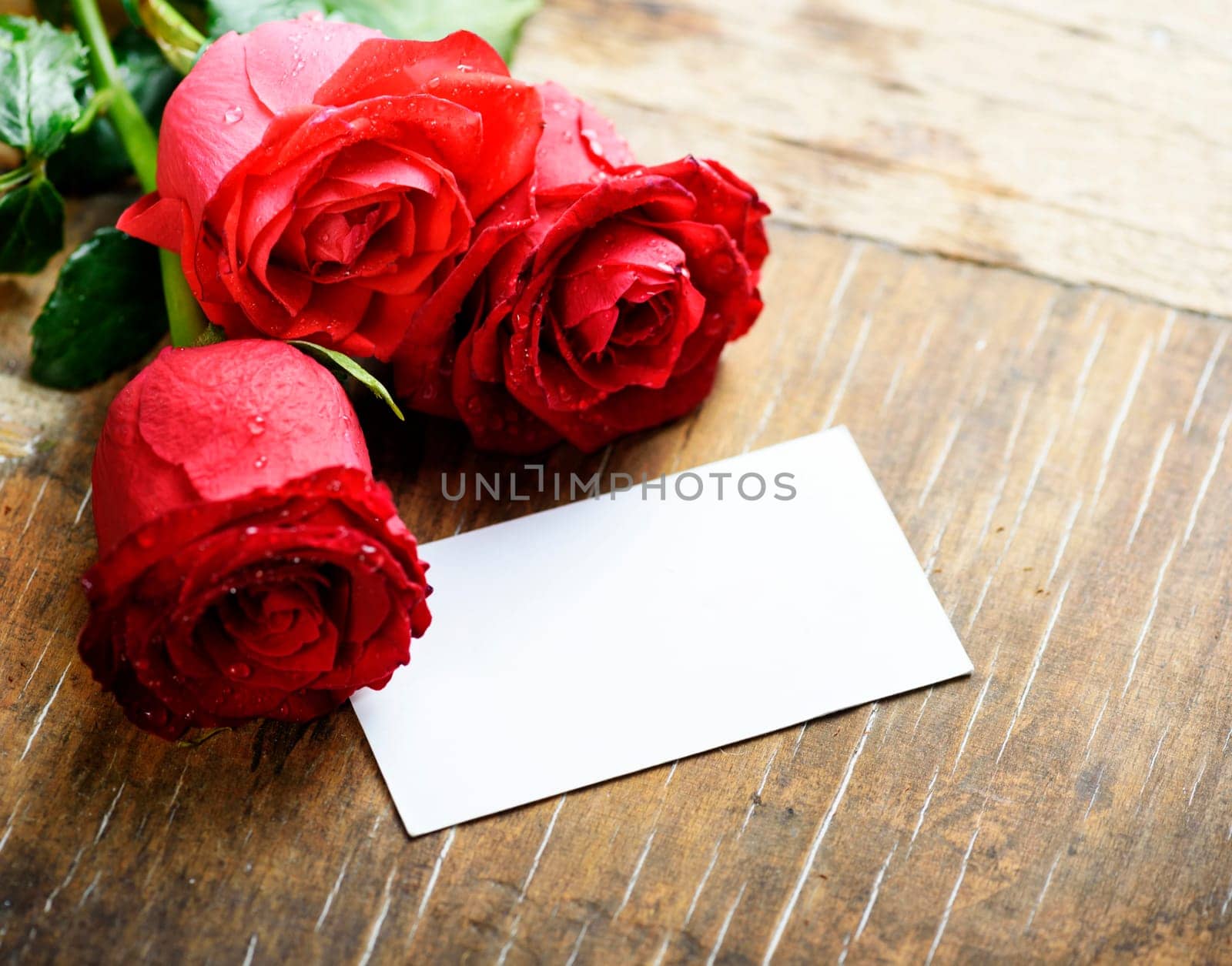 Red roses with empty card on wooden table. Valentine concept.