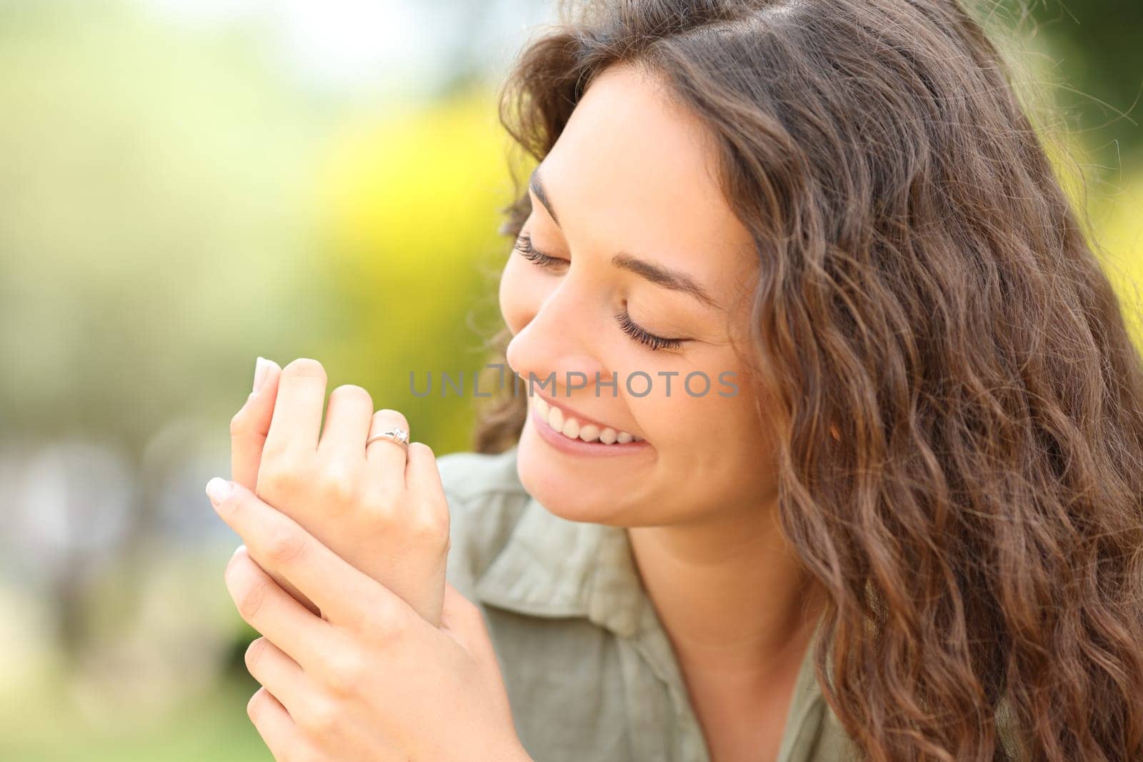 Happy woman looking at wedding ring after engagement in a park