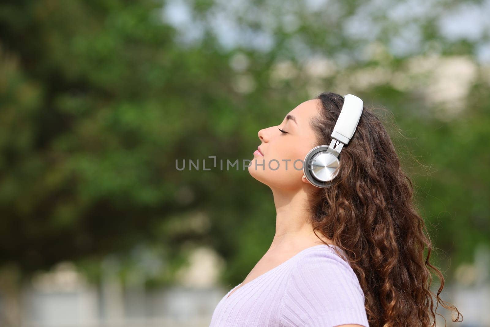 Side view portrait of a relaxed woman wearing headphones listening audiobook meditating in a park