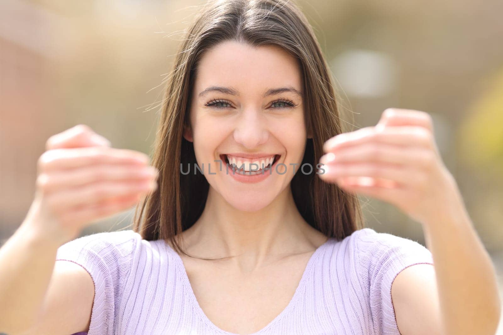 Front view portrait of a happy teen saying come here with both hands at camera in a park