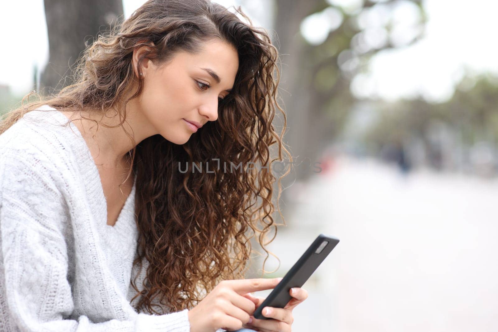 Serious woman using cell phone sitting on a bench in the street