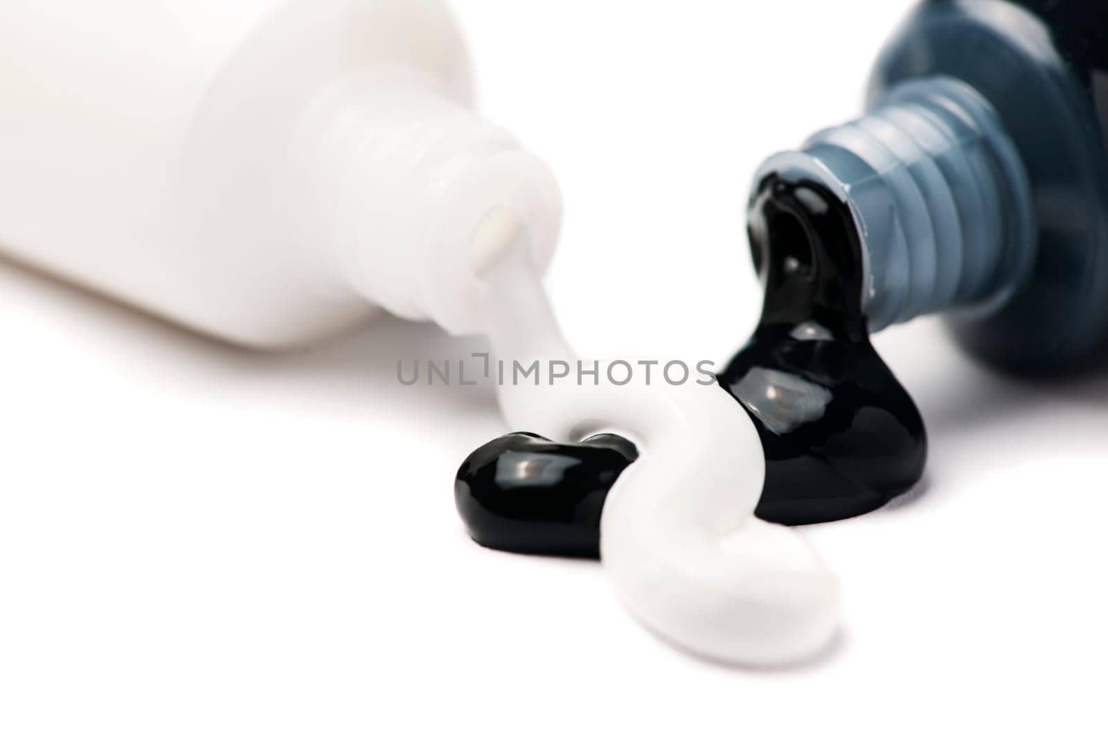 Close-up of two open tubes of artist paint with black and white acrylic paint pouring out on a white background.