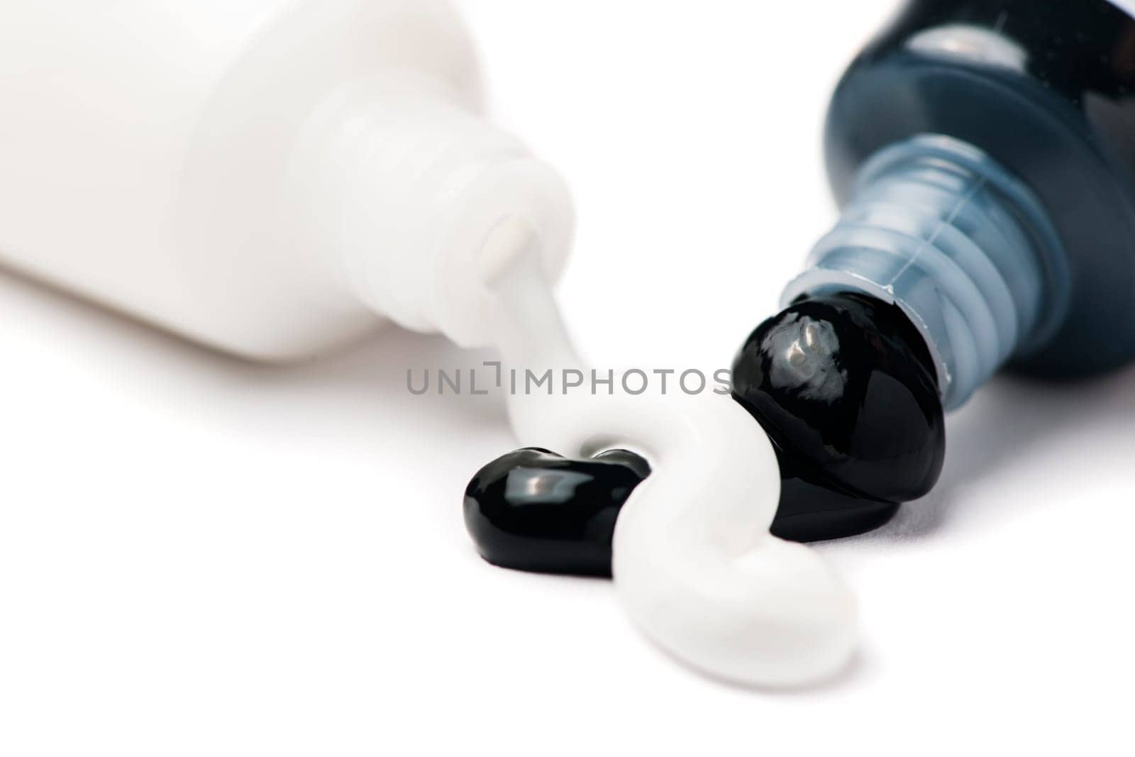 Close-up of two open tubes of artist paint with black and white acrylic paint pouring out on a white background.