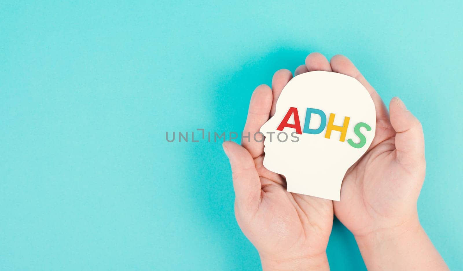 Hands holding a head with the german word ADHS which means attention deficit hyperactivity disorder, ADHD symptom, mental health