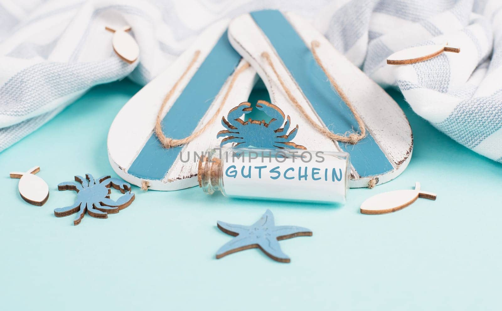 Blue colored summer and vacation background, flip flops, sea stars and a glass bootle with the word coupon in german language, holiday, travel and tourism concept