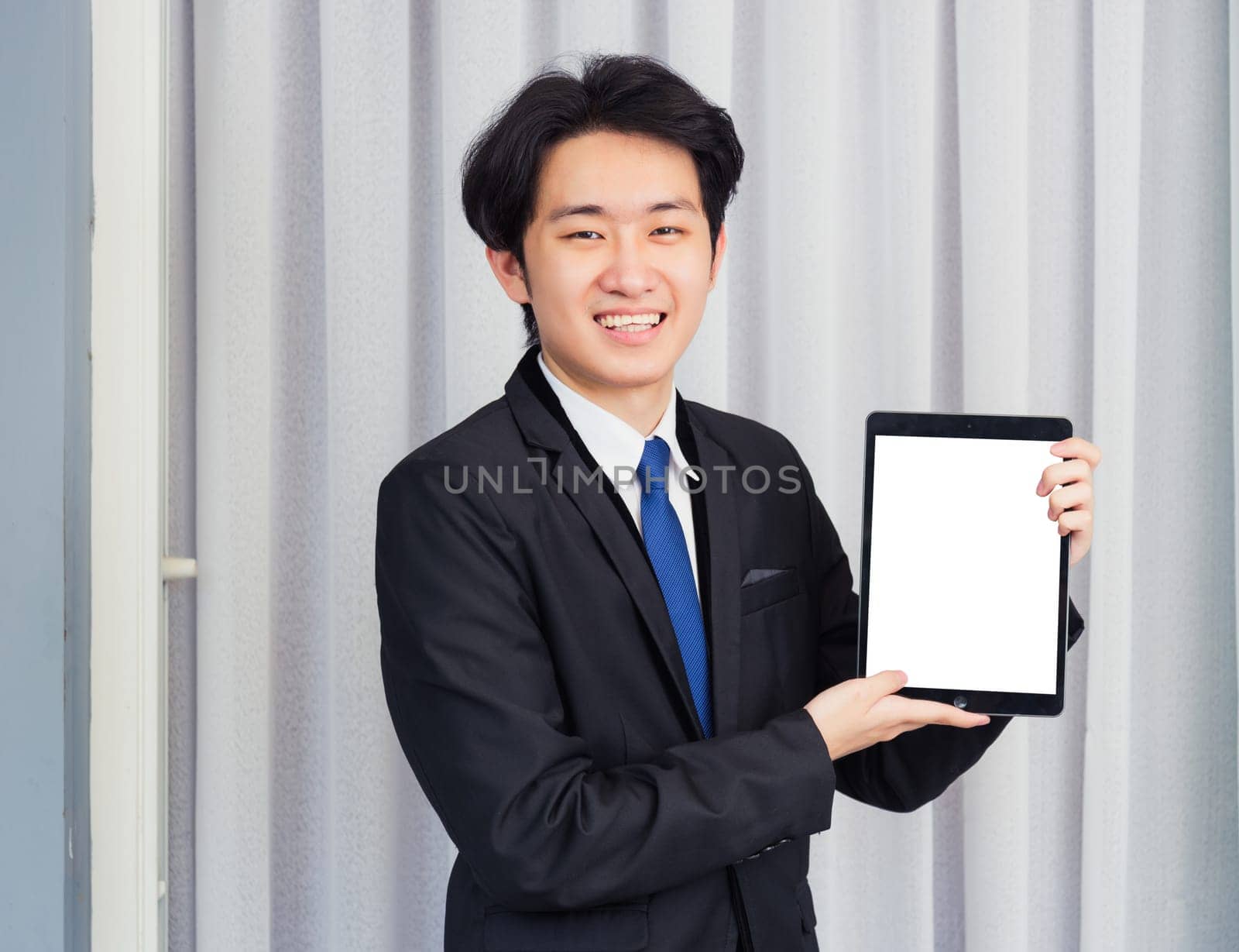Work from home, Asian young businessman wear suit video conference call or facetime he smiling and showing blcnk screen of smart digital tablet computer at home office, looking to camera