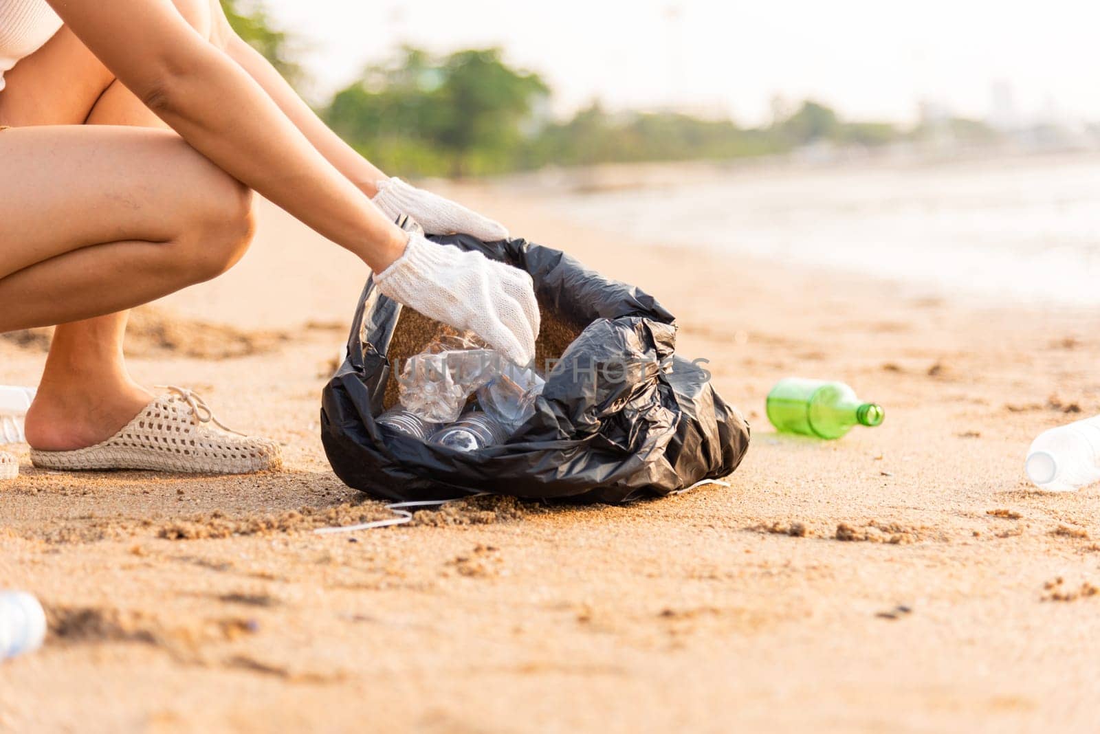 Volunteer woman picking plastic bottle into trash plastic bag black for cleaning the beach, female clean up garbage at sunset, Ecology concept and World Environment Day, Save earth concept