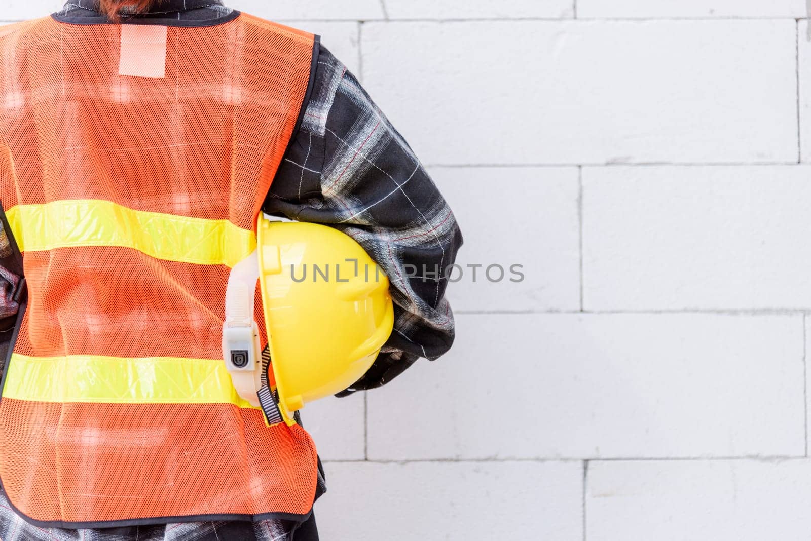 Back view of engineer, architect, supervisor worker wear reflective clothing for the safety of the work operation hold safety helmet in vest standing at wall building construction site