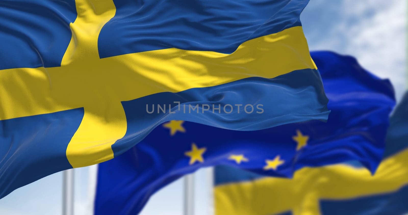 Detail of the national flag of Sweden waving in the wind with blurred european union flag in the background on a clear day. Democracy and politics. European country. Selective focus.