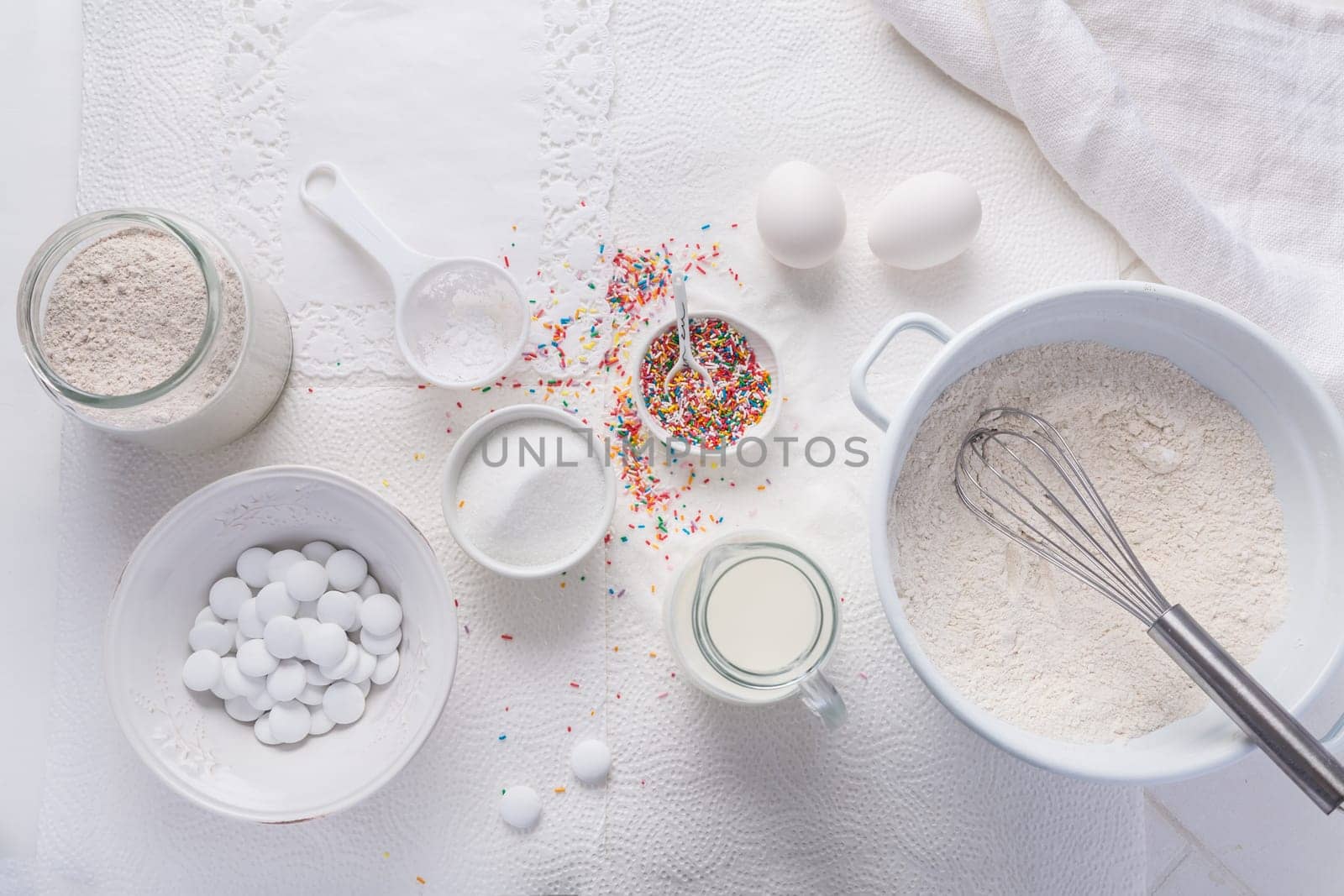 Baking background with flour, eggs, sugar sprinkles, kitchen tools, utensils in white