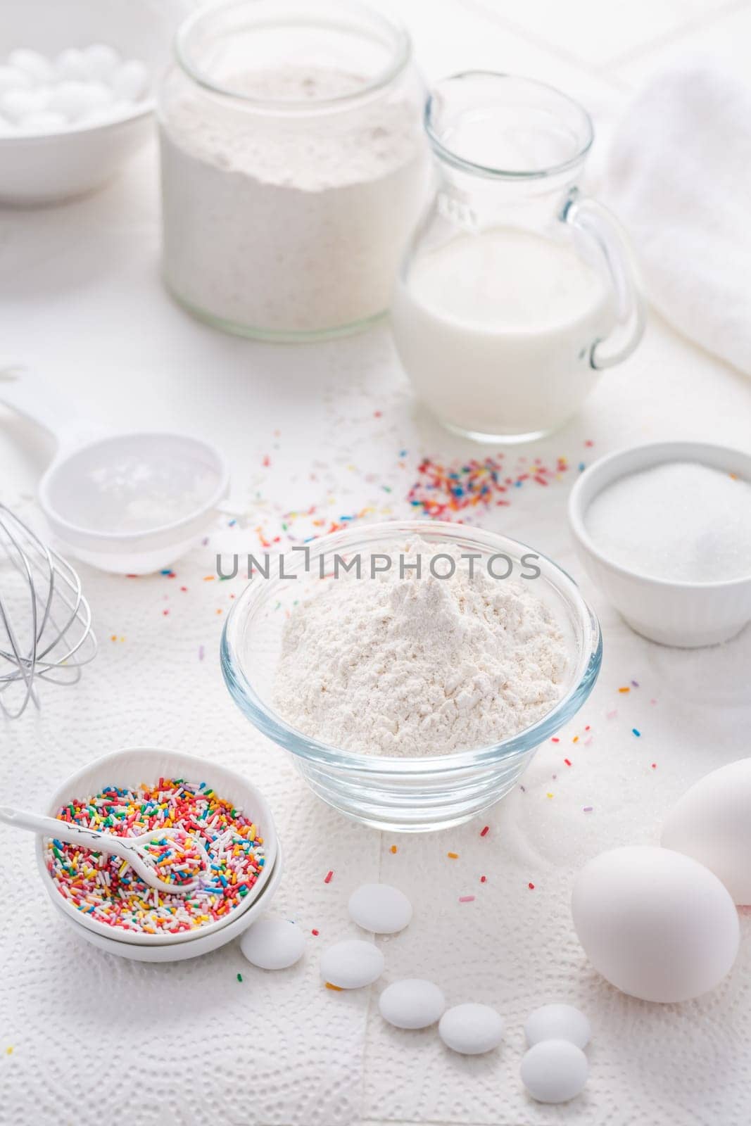 Baking background with flour, eggs, sugar sprinkles, kitchen tools, utensils in white