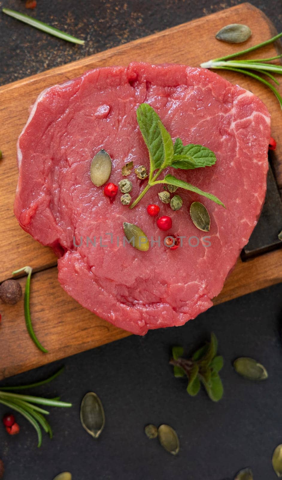 Raw beef fillet steak on wooden board on dark table top view. Portioned filet mignon with spices and herbs. Concept of summer food