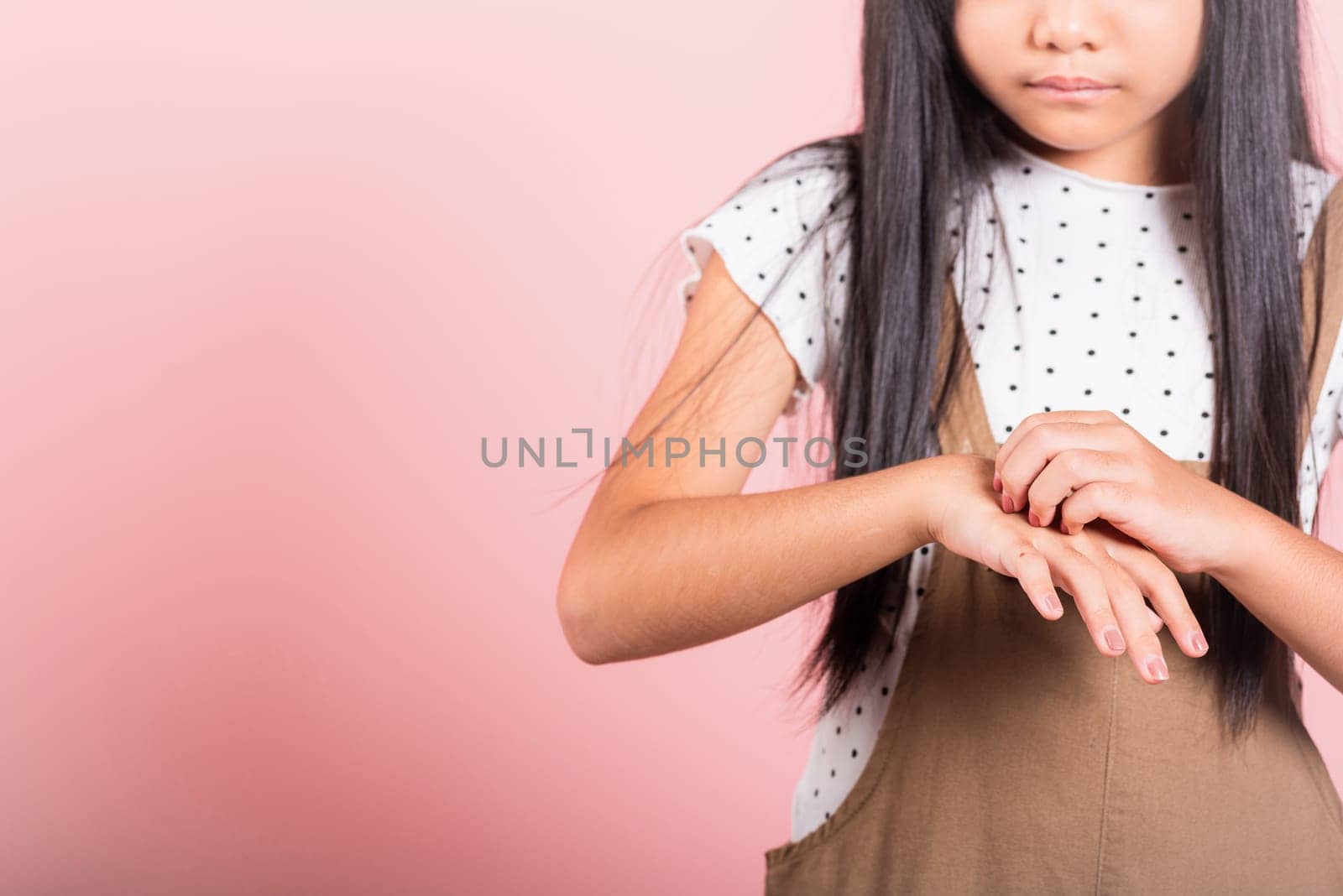 Asian little kid 10 years old scratching itch back hand from mosquito bite at studio shot isolated on pink background, Child girl dermatitis and scabies, Allergy symptoms, healthcare and medicine