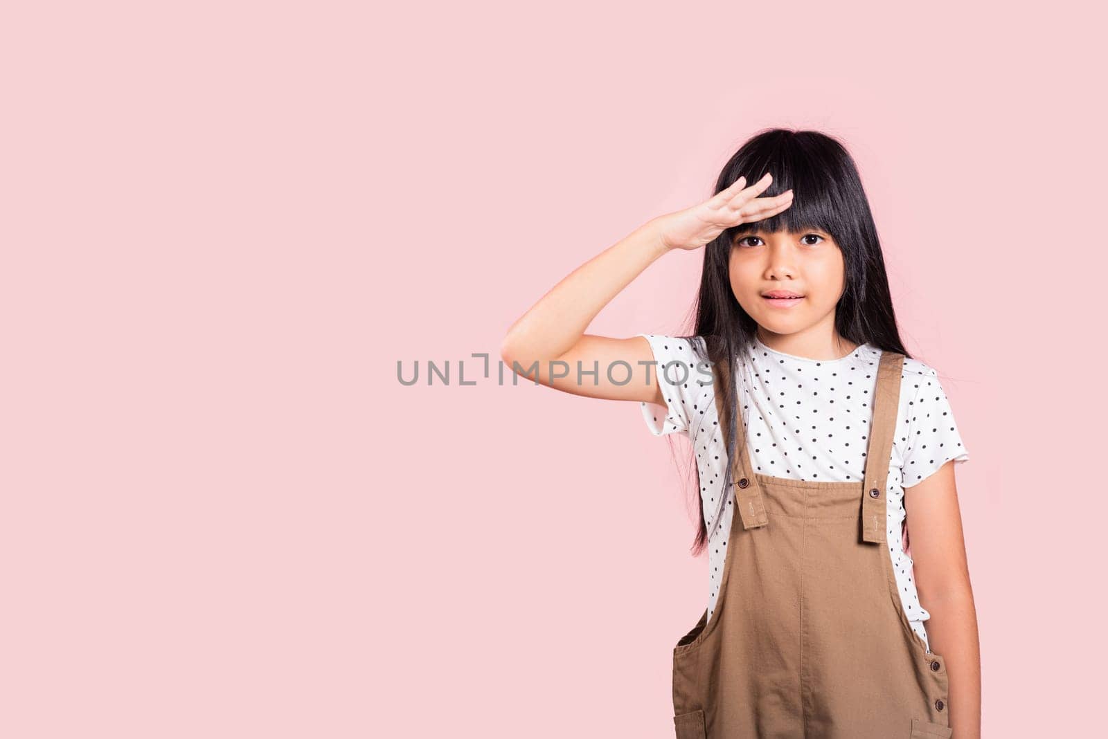 Searching concept. Asian little kid 10 years old looking far away with hand over head at studio shot isolated on pink background, Portrait of Happy child girl looking at distance with eyes shaded